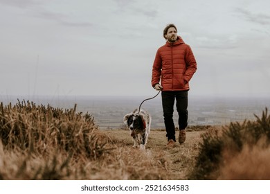 Mature white man walking dog on outdoor nature hill. Caucasianman in red down jacket walking with dog through nature hill. Middle aged Caucasian man travel with his dog in nature. - Powered by Shutterstock