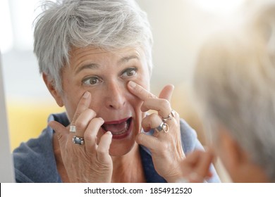 Mature White-haired Woman Checking Eye Wrinkles In Front Of Mirror