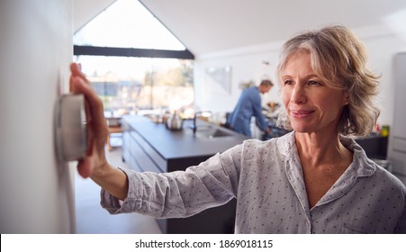 Mature Woman Adjusting Wall Mounted Digital Central Heating Thermostat Control At Home