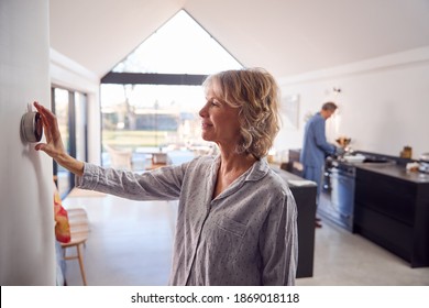 Mature Woman Adjusting Wall Mounted Digital Central Heating Thermostat Control At Home - Powered by Shutterstock