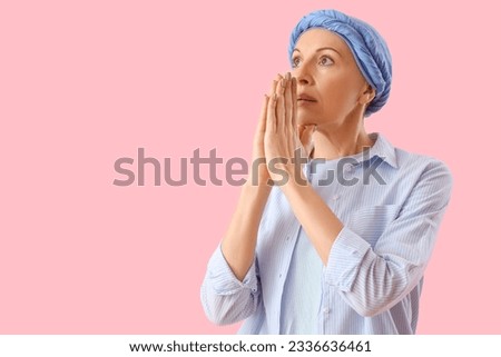 Mature woman after chemotherapy praying on pink background