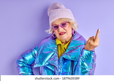 mature woman with an angry facial expression shows fuck you. the concept of discontent and protest of old woman isolated purple background