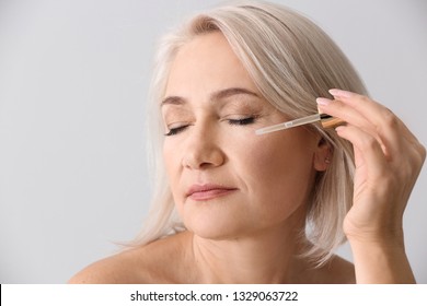 Mature Woman Applying Face Serum On Light Background