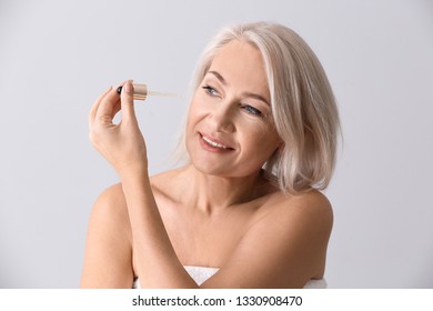 Mature Woman Applying Face Serum On Light Background