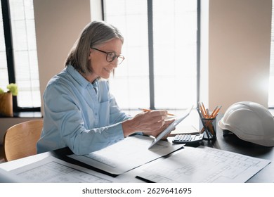 Mature woman, architect and blueprint with tablet, planning and design for vision or project. Female person, professional and technology as designer or creative for management, company or development