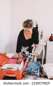 Mature Woman Arriving At The Hotel Room And Unpacking Her Luggage. Summer Trip, Weekend. Concept Leisure And Hobby.