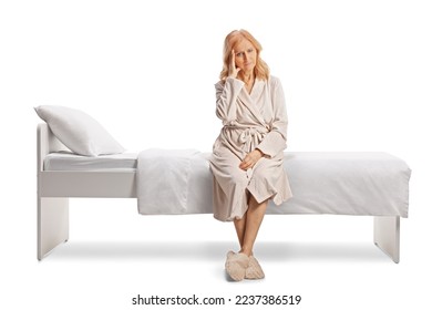 Mature woman in a bathrobe sitting on a bed and holding her head isolated on white background - Powered by Shutterstock