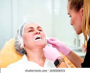 Mature Woman At A Beautician Appointment. Applying Anesthetic Cream To The Lips.