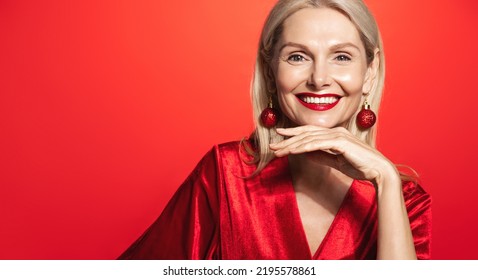 Mature woman with beautiful red lipstick and christmas earring, smiling and looking happy at camera, touching glowing and nourished facial skin after skincare cosmetics - Powered by Shutterstock