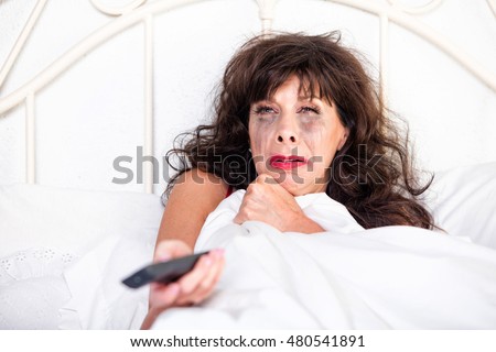 Mature woman in bed watching something sad on television