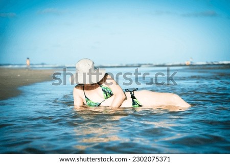 Mature woman in a bikini and hat bathing in the sea on a sunny day. Taquari, Guaibim beach, Valenca, Bahia.