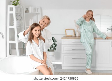 Mature woman brushing her little granddaughter's hair in bathroom - Powered by Shutterstock