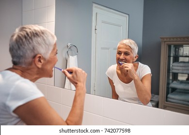 Mature Woman Brushing Her Teeth In The Bathroom.