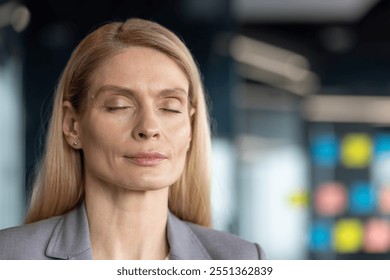 Mature woman businesswoman with closed eyes in office setting, embracing calmness, focus, mindfulness. Portrays serenity, meditation, tranquility at workplace. - Powered by Shutterstock