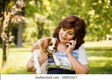 Mature Woman Calling Phone While Holding Her Dog By Outdoor In Nature