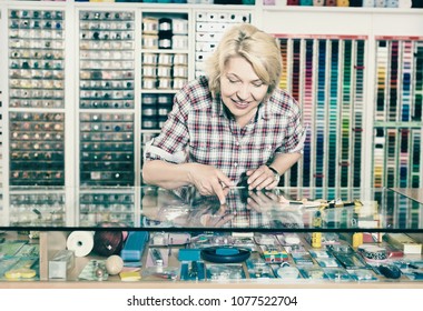 Mature Woman Cashier Showing On Shop Display Sewing Tools For Hobby In Craft Shop