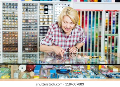 Mature Woman Cashier Showing On Shop Display Sewing Tools For Hobby In Craft Shop