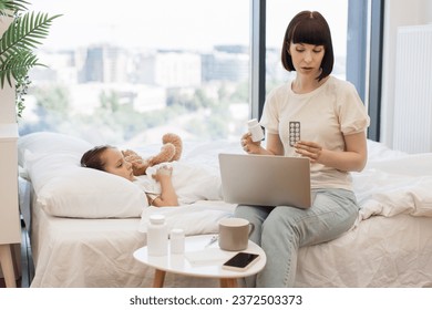 Mature woman in casual wear talking to competent pediatrician during video call on modern laptop. Good mother sitting on bed and taking advices about pills while caring of cute little daughter. - Powered by Shutterstock