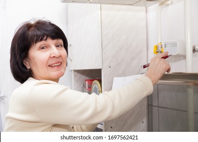 Mature Woman Checking   Gas Meter In   Kitchen. 