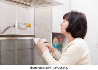 Mature Woman Checking   Gas Meter In   Kitchen. 