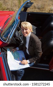 Mature Woman With Classic Red Convertible Car On Road Trip Using Map