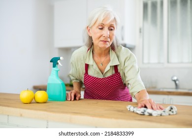 Mature woman cleaning table with cloth and spray at kitchen. Everyday household chores concept - Shutterstock ID 2184833399