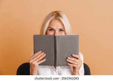 Mature woman covering her face while sitting in chair isolated over beige background - Powered by Shutterstock