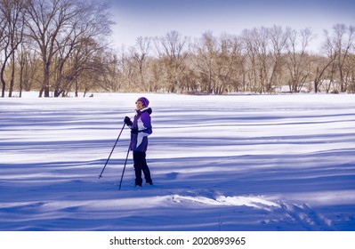 Mature Woman Cross-country Skier Enjoying Fresh Snow In Late Afternoon In Midwest; Long Shadows Around Her