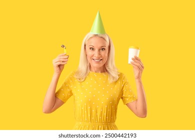 Mature woman with cup of coffee celebrating birthday on yellow background - Powered by Shutterstock