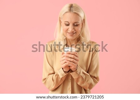 Mature woman with cup of coffee on pink background