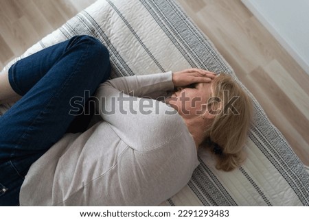 Mature woman curled lying on the bed at home top view. Depression, mental health, abuse problem