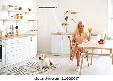 Mature Woman And Cute Labrador Dog In Kitchen With Switched On Air Conditioner