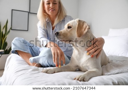 Mature woman with cute Labrador dog sitting on bed at home