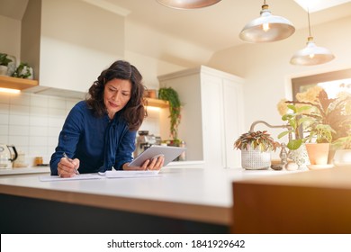 Mature Woman With Digital Tablet Reviewing Domestic Finances And Paperwork In Kitchen At Home - Shutterstock ID 1841929642
