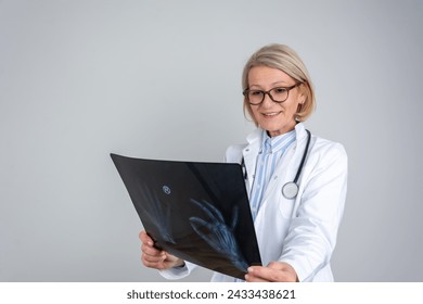 Mature woman doctor isolated looking at X-ray results. Medicine, radiology and healthcare concept. Positive senior female doctor in white coat and glasses reading x ray  - Powered by Shutterstock