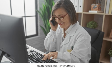 Mature woman doctor multitasks, typing on computer while speaking on the phone in her office. - Powered by Shutterstock