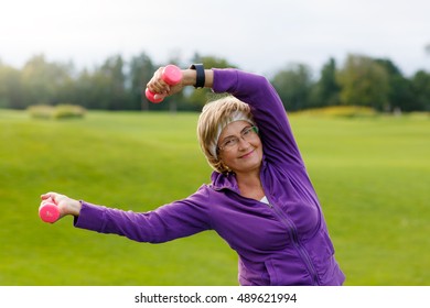 Mature Woman Doing Exercises With Dumbells At Park In Evening