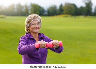 Mature Woman Doing Exercises With Dumbells At Park In Evening