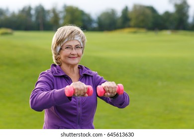 Mature Woman Doing Exercises With Dumbells At Park In Evening