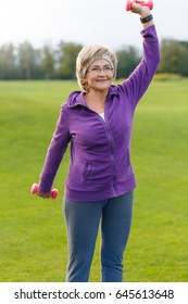 Mature Woman Doing Exercises With Dumbells At Park In Evening