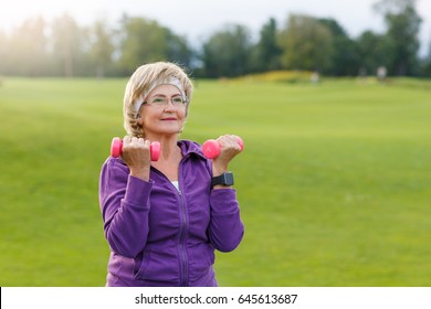 Mature Woman Doing Exercises With Dumbells At Park In Evening