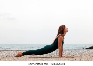 Mature woman doing Urdhva mukha shvanasana yoga exercise, upward facing dog pose, stretching back muscles, working out at the beach wearing sportswear, outdoor full length. Copy space - Powered by Shutterstock