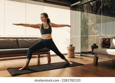 Mature woman doing the warrior pose during a session of yoga. Senior woman doing a balance exercise on an exercise mat. Active woman practicing a healthy fitness routine at home. - Powered by Shutterstock