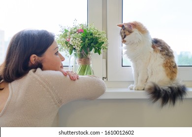 Mature Woman And Domestic Tricolor Cat Sitting On The Window, Owner Watching And Talking With Pet