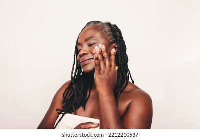 Mature Woman With Dreadlocks Applying Moisturizing Cream On Her Face. Confident Dark-skinned Woman Taking Care Of Her Flawless Melanated Skin. Mature Black Woman Ageing Gracefully.