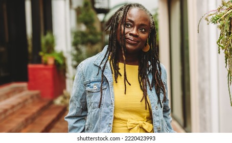 Mature woman with dreadlocks looking away thoughtfully while standing outdoors. Senior woman going out in casual clothing.