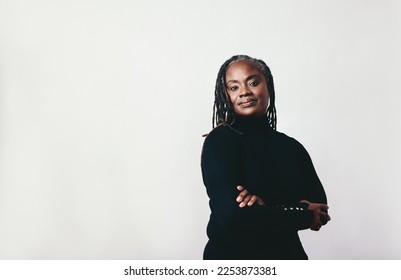 Mature woman with dreadlocks looking at the camera in a studio. Elegant middle-aged woman standing against a grey background with her arms crossed. - Powered by Shutterstock