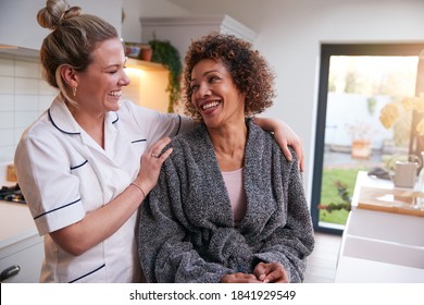 Mature Woman In Dressing Gown Talking With Female Nurse In Kitchen At Home