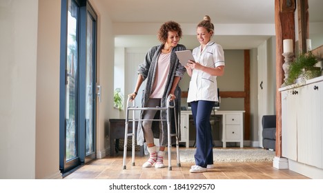 Mature Woman In Dressing Gown Using Walking Frame Being Helped By Female Nurse With Digital Tablet - Powered by Shutterstock