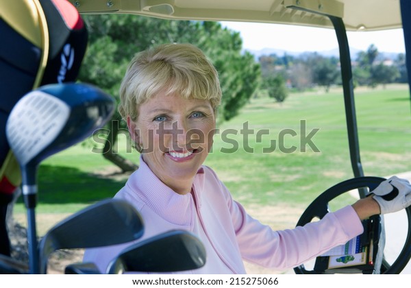 Mature woman driving golf buggy on golf course,\
smiling, side view,\
portrait